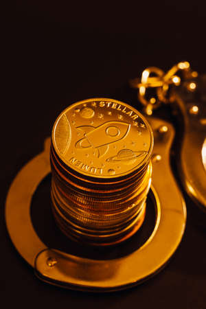 Stack of Stellar lumen coins and handcuffs over black background