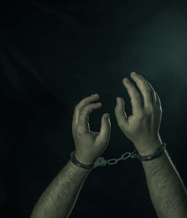 Male hands in handcuffs over dark backgroundの写真素材