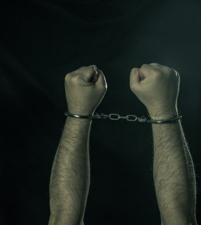 Male hands in handcuffs over dark background