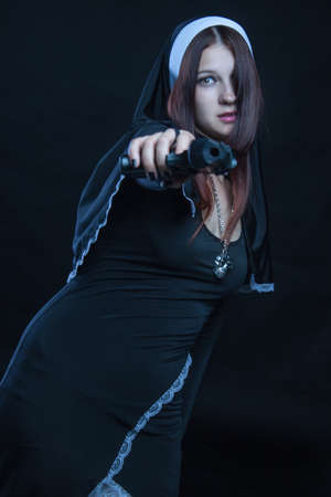 Seductive nun with gun posing over dark backgroundの写真素材