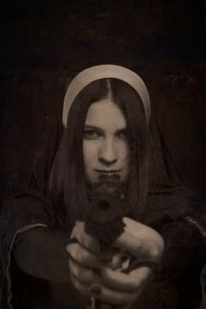 Seductive nun with gun posing over dark backgroundの写真素材