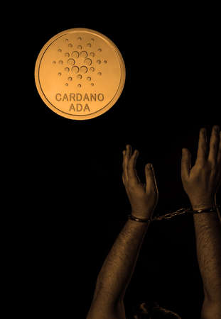 Hands in handcuffs and cardano coin over dark background. Crypto crime concept.
