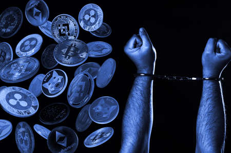 Hands in handcuffs and cryptocurrencies over dark background. Crypto crime concept.