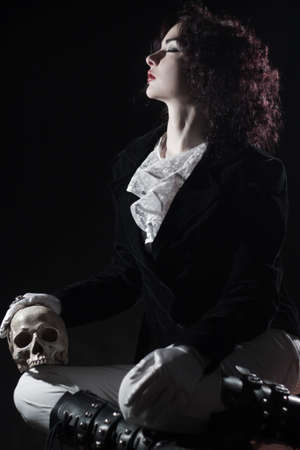 Pretty old fashioned girl posing with skull over dark background