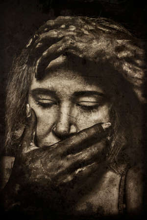 Woman embracing her head by her hands over dark backgroundの写真素材