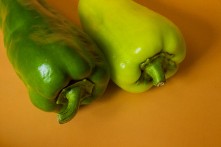 Close-up shot of two green peppers over yellow backgroundの写真素材