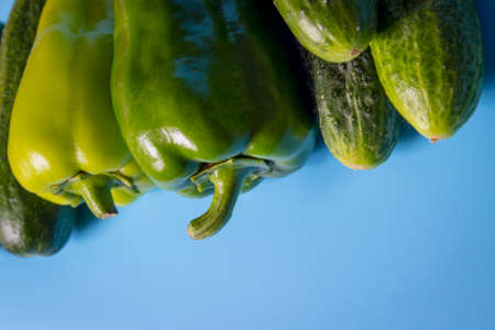 Close-up shot of two green peppers and cucumbers over blue background