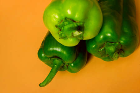 Close-up shot of three green peppers over yellow background