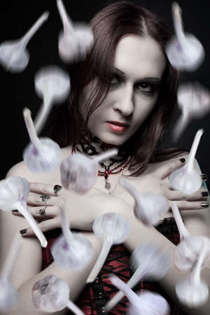 Pretty vampire in red corset and a lot of garlic bulbs falling from aboveの写真素材
