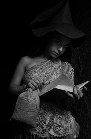 Pretty girl in witch hat posing with book over dark backgroundの写真素材