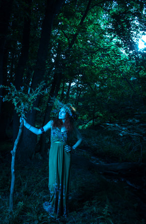 Redhead beautiful lady in green dress posing in the forestの写真素材