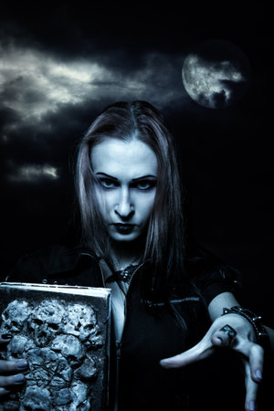 Gothic redhead girl with old grunge horrible book posing over dramatic sky. Photo of the moon: NASA.の写真素材