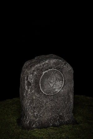 Tombstone with ethereum symbol in green grass over black background.