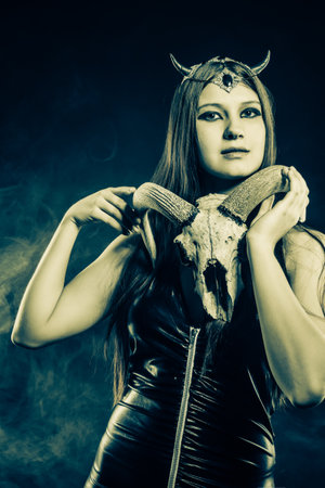 Sexy mistress in latex posing over dark background with skull