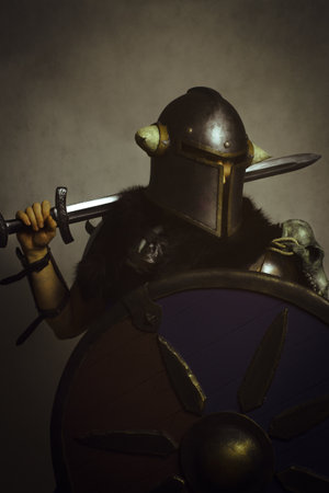 Northern warrior in helmet with sword and shield posing over grey backgroundの写真素材