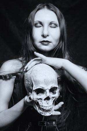Gothic girl with skull posing over dark background