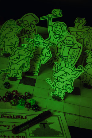 Hand-drawn fantasy tabletop role-playing game scene with paper miniatures of goblins and adventurers, including a wizard, paladin, warrior, and rogue. The figures are placed on a grid battle map with colorful d20 scattered around, creating a vivid and creative RPG atmosphere.の写真素材