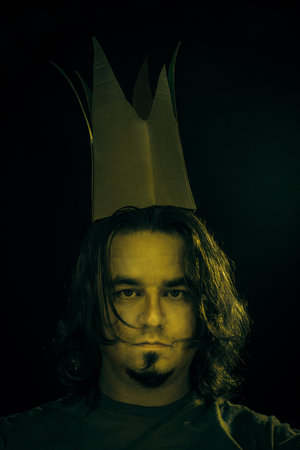 Young man in cardboard fake crown over dark background.