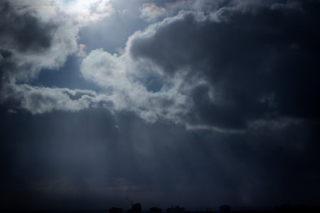 Dramatic dark storm clouds with powerful sun rays breaking through, creating a moody and atmospheric...