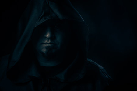 Dark moody portrait of a mysterious hooded man emerging from shadows. Low-key cinematic lighting...
