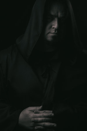 Dark moody portrait of a mysterious hooded man emerging from shadows. Low-key cinematic lighting...