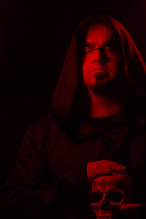 Dark moody portrait of a mysterious hooded man emerging from shadows. Low-key cinematic lighting...