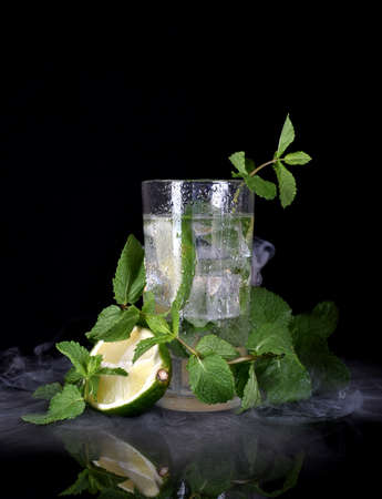 Glass of Mojito cocktail with ice cubes mint and lime on black background with fresh lime. Sparkling refreshing water.の写真素材
