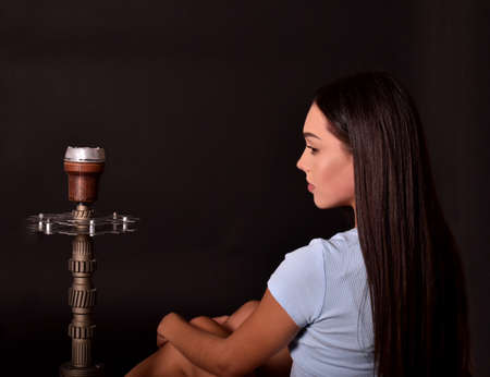 The girl smokes a hookah on a black background. Smoke comes out of the mouth. The pleasure of smokingの写真素材