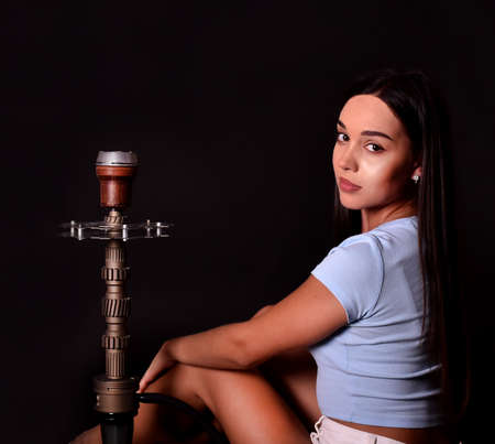 The girl smokes a hookah on a black background. Smoke comes out of the mouth. The pleasure of smokingの写真素材