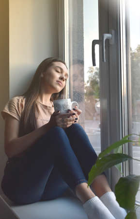 the girl sits on the windowsill and drinks coffeeの写真素材