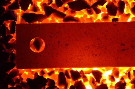 Background of burning coal anthracite and a red-hot steel strip with a hole.