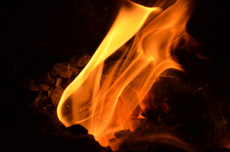 Burning flame bursts out of the hole between the coals.