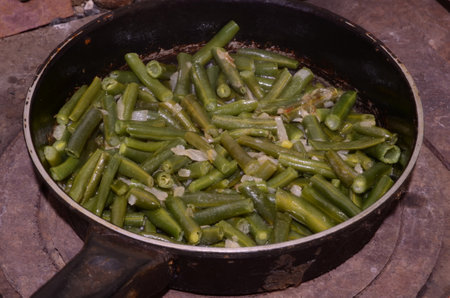 Chopped beans are fried in an old frying pan.の写真素材