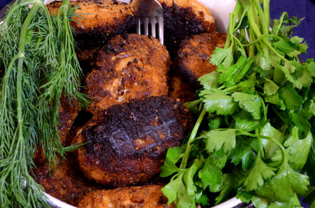 Meat cutlets lie on a dish between bunches of dill and parsley.