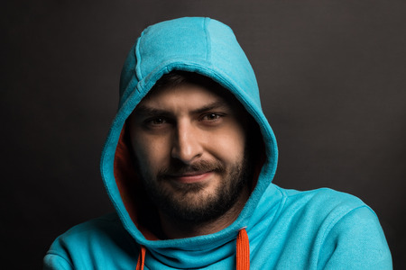 Low key  portrait of a serious  man with a thick beard wearing blue  in hooded jacket and looking at the cameraの写真素材