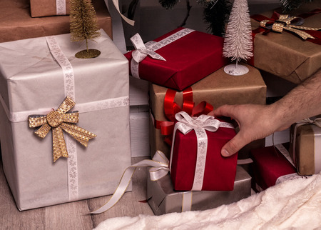 Hand of man putting or taking  Christmas gift . Decorated christmas tree and bunch of gifts on...