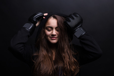 Young female model wearing sports hooded sweatshirt and boxing gloves. Black backgroundの写真素材