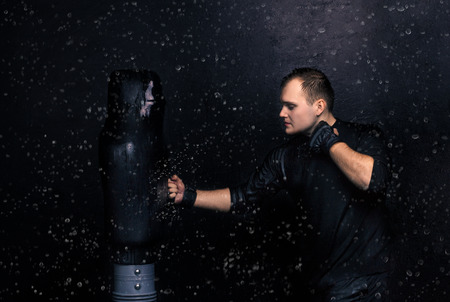 Portrait of boxer hitting the dummy in the rain. droplets bounce off the treadmill. Aquastudio shot.の写真素材