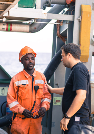 friendship of nations on board of ship/vessel. European Chief officer instructing African seaman on deck before job.の写真素材