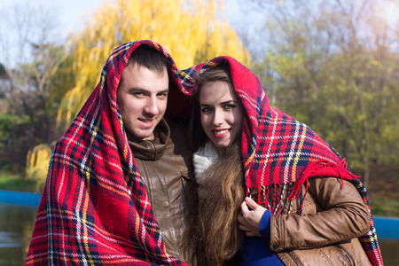 Young couple sitting on bench at the park covered in heart shaped plaid/blanket. Sunny autumn season.の写真素材