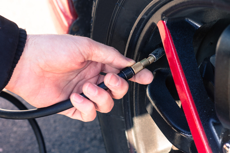 Man connecting air compressor to car tires for checking air pressure and filling with airの写真素材