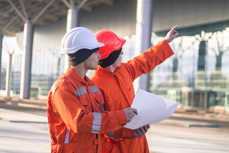 team of  young engineers discussing a construction project. The wear overalls and safety helmets. Business modern backgroundの写真素材
