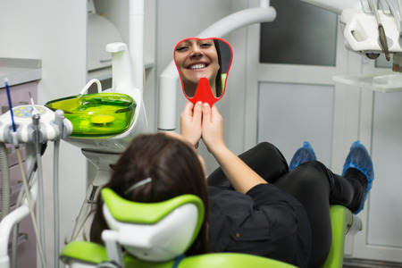 young smiling woman looking at mirror reflection  in the dentists chair. の写真素材