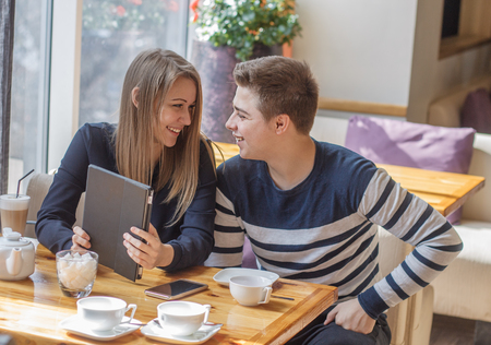 Cheerful couple dating in a cafe. They are having fun and smiling with tablet.  they are looking at each otherの写真素材