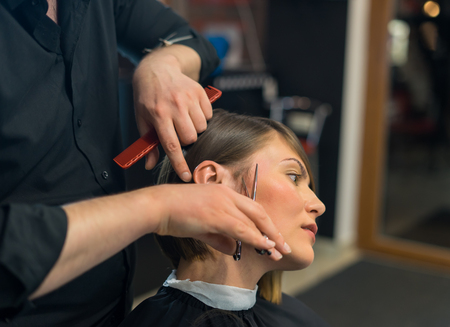 Male hairdresser does a haircut to pretty woman in the beauty salon.の写真素材