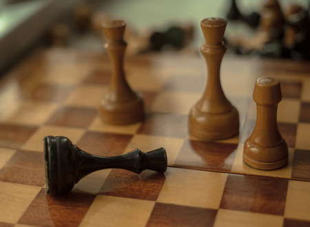 Chess game. Black king is checkmated and fallen on chessboard. game over. Old wooden chessの写真素材