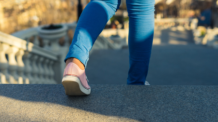 Young girl is walking downstairs on ladder. Step down. She is wearing sneakers. business or education conceptの写真素材