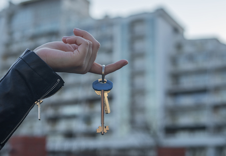 Hand holding key with modern building on background. Buying new home or flat concept.
