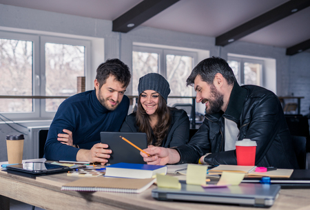 Young smart team. Group of  modern people discussing work on tablet in the office. Working environment with laptop, coffee, notepads and stationery. They are looking at the screen. Business team concept.の写真素材