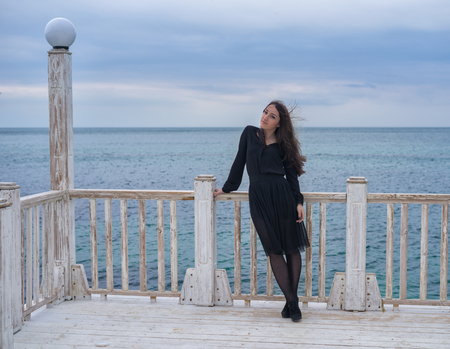 brunette girl in a black dress posing on the pierの写真素材